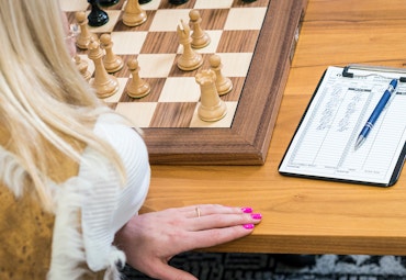 back of a woman with blond hair detail of hand with pink nails and chess board
