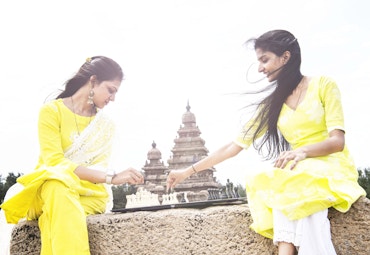 two woman playing chess in indian wearing yellow clothes in front of a building